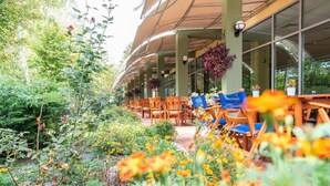 An outdoor seating area with tables and chairs, surrounded by a garden with various plants and flowers. - Hotel Ivana Palace (Sunny Beach)