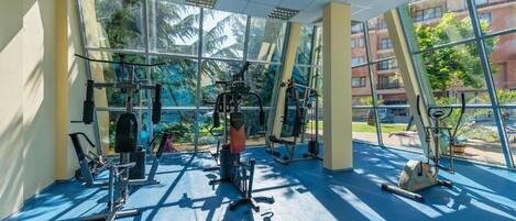 A gym with various exercise machines, large windows, and a blue floor.