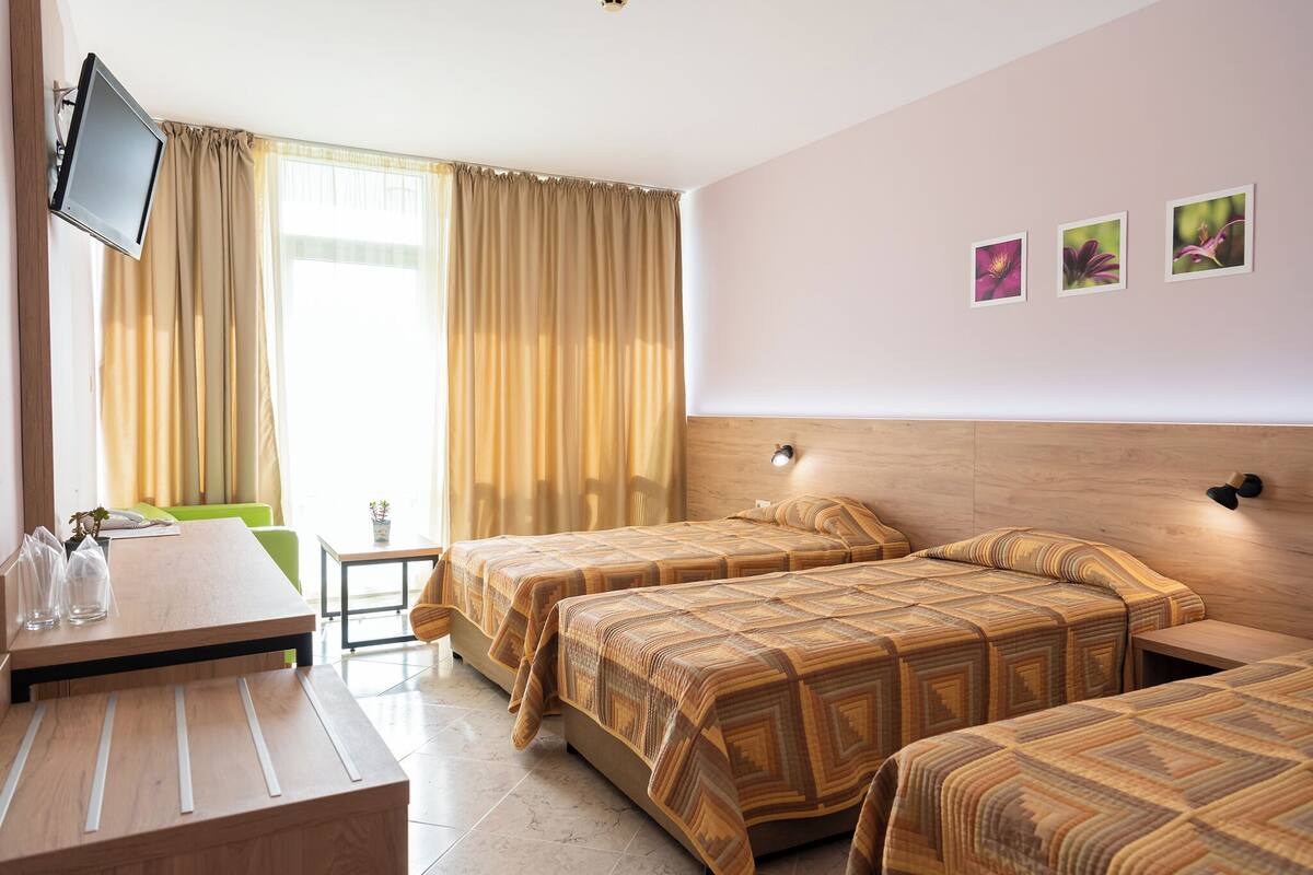 A hotel room with two beds, a desk, a TV, and a window with curtains.