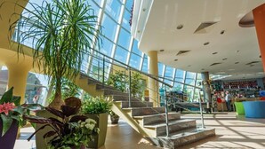 A spacious atrium with a staircase, potted plants, and a view of the outside through large windows. - Hotel Ivana Palace (Sunny Beach)