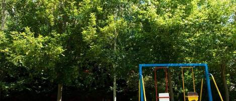 A playground with swings and a blue frame, surrounded by trees.