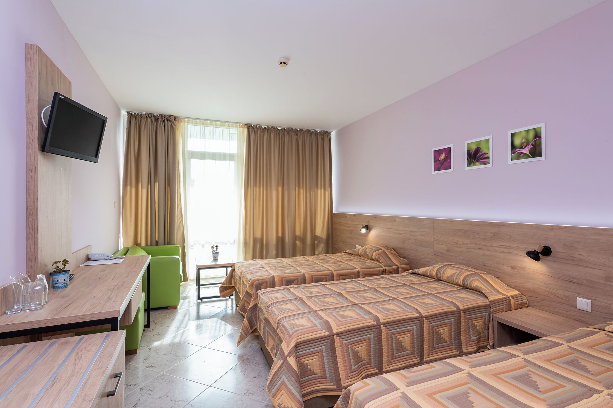 A hotel room with two beds, a desk, a TV, and a window with curtains.