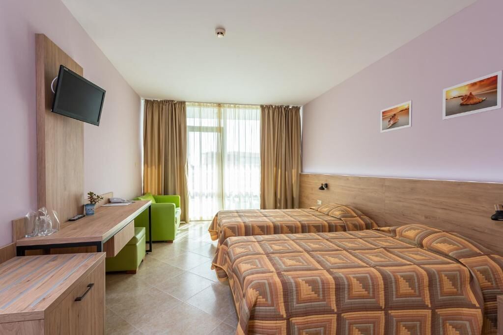 A hotel room with two beds, a desk, a television, and a window with curtains.