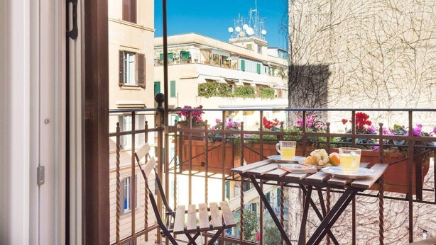 A balcony with a table set for two, a chair, and a view of neighboring buildings.