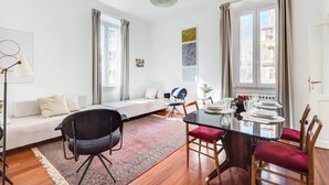 A modern living room with a sofa, a dining table set for four, and a chandelier.