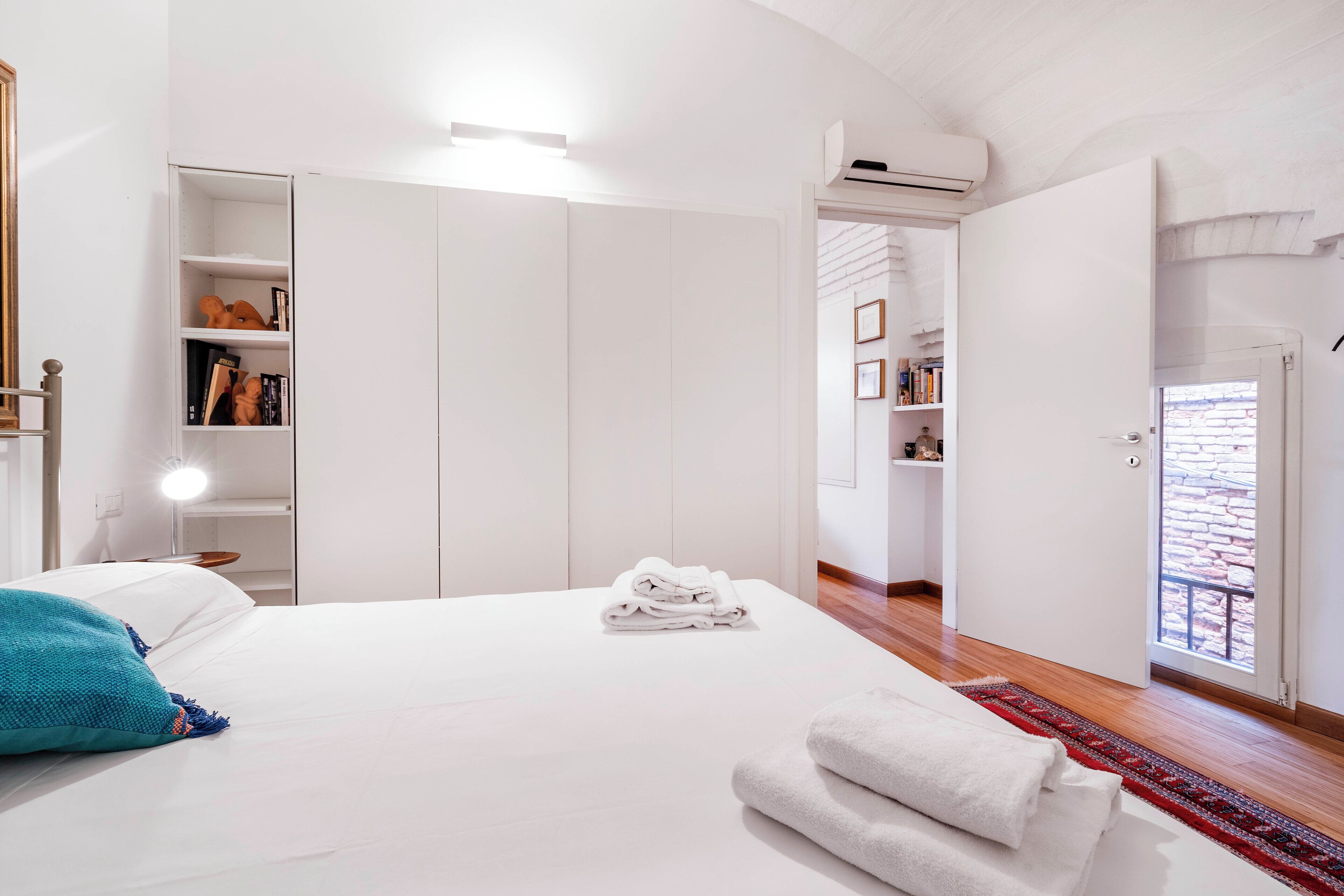 A bedroom with a neatly made bed, a white wardrobe, and a door leading to a balcony.