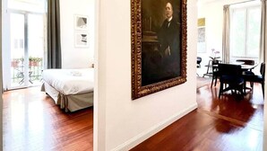 Een ruime kamer met een groot bed, een eethoek en een schilderij aan de muur.