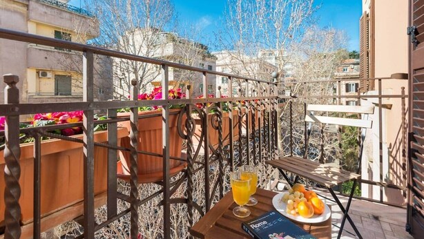 Een balkon met een tafel gedekt voor het ontbijt, inclusief een bord met fruit en glazen sinaasappelsap.