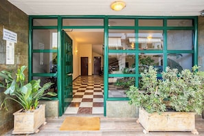 A hotel entrance with a checkered floor, green-framed glass doors, and potted plants.
