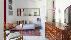 A compact living space with a bed, a dining table with chairs, a TV on a wooden cabinet, and a mirror on the wall. - Glorioso Marble | Trastevere ArtDesignApartments (Roma)