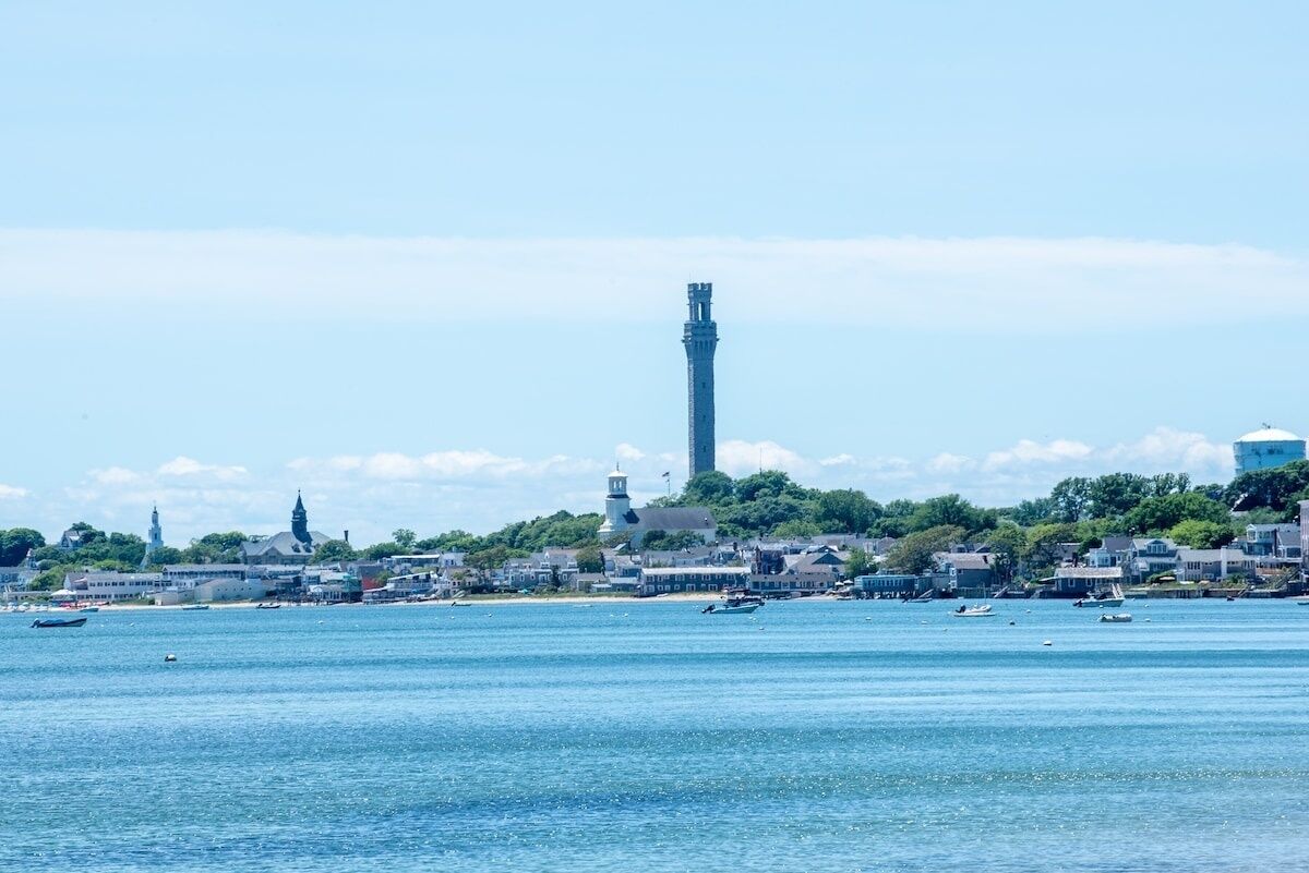 A coastal cityscape with a prominent tower, calm water, and buildings along the shore.
