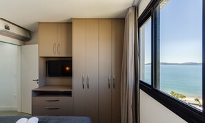 Une chambre d’hôtel avec un lit, une télévision, une armoire et une fenêtre donnant sur la mer.