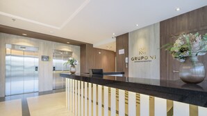 Egy modern recepciós pult, rajta a cég logója, egy virágos váz és két lift.