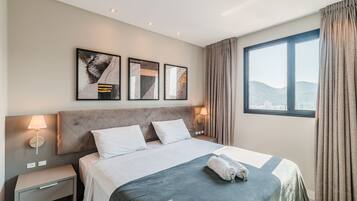 A hotel room with a bed, nightstand, wall art, and a window with curtains.