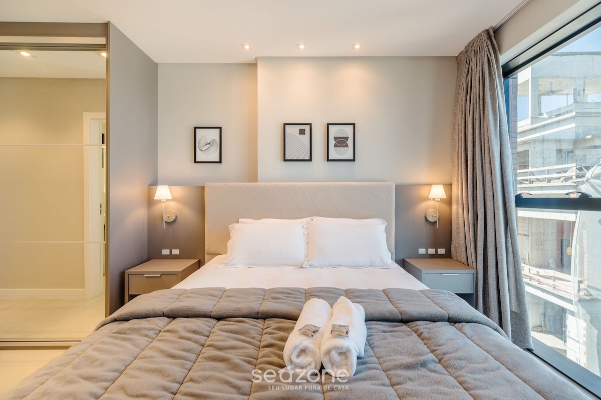 A modern hotel room with a large bed, two bedside lamps, and a window with a view of the city.
