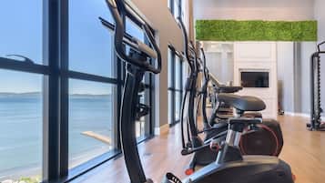 Un gimnasio con equipo de ejercicio, ventanas amplias y vista al mar.