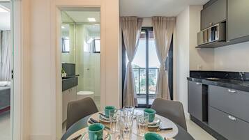 Una cocina moderna con armarios oscuros, una mesa de comedor con platos verdes y vasos transparentes, y vistas de la ciudad a través de amplios ventanales.