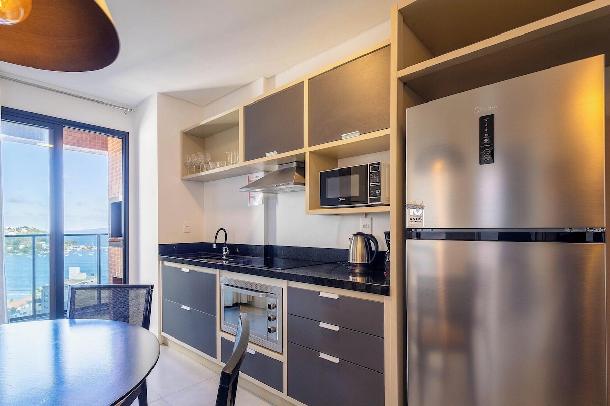 A modern kitchen with a built-in microwave, stainless steel refrigerator, and a dining area with a view of the sea.