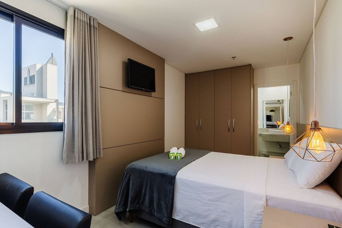 A hotel room with a bed, a desk, a chair, a TV, and a window with curtains.