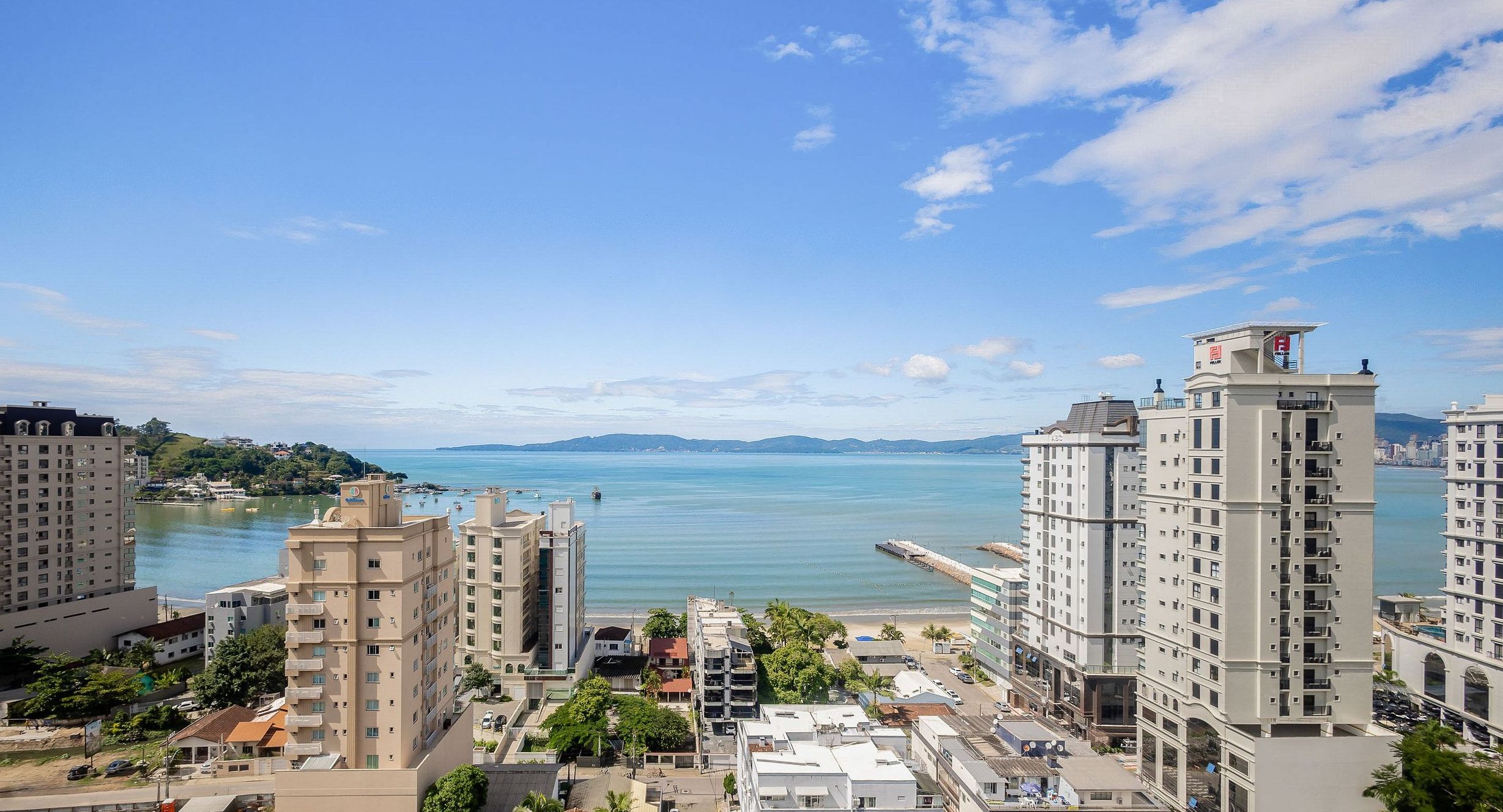 Un paysage urbain côtier avec de hauts immeubles, un ciel dégagé et une mer calme.