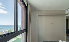 Quarto com uma janela grande, porta e vista para o mar e edifícios.