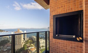 Un balcon donnant sur la mer et les bâtiments, un mur en briques et un gril noir.