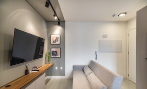 Een moderne woonkamer met een flatscreen televisie, een houten salontafel, een grijze bank en abstracte wanddecoratie.