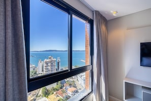 A room with a large window, a flat-screen TV, and a white shelf.