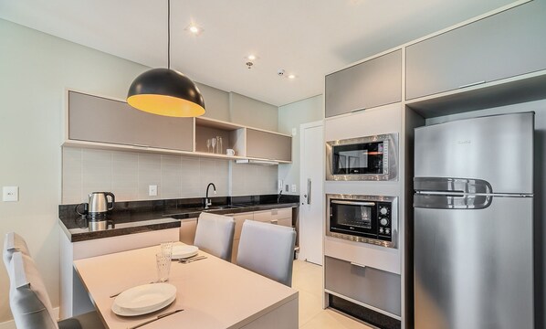 A modern kitchen with built-in appliances, a dining area, and a pendant light. - MHF II Apts Variados em Prédio com Vista para o Mar em Itapema (Itapema)