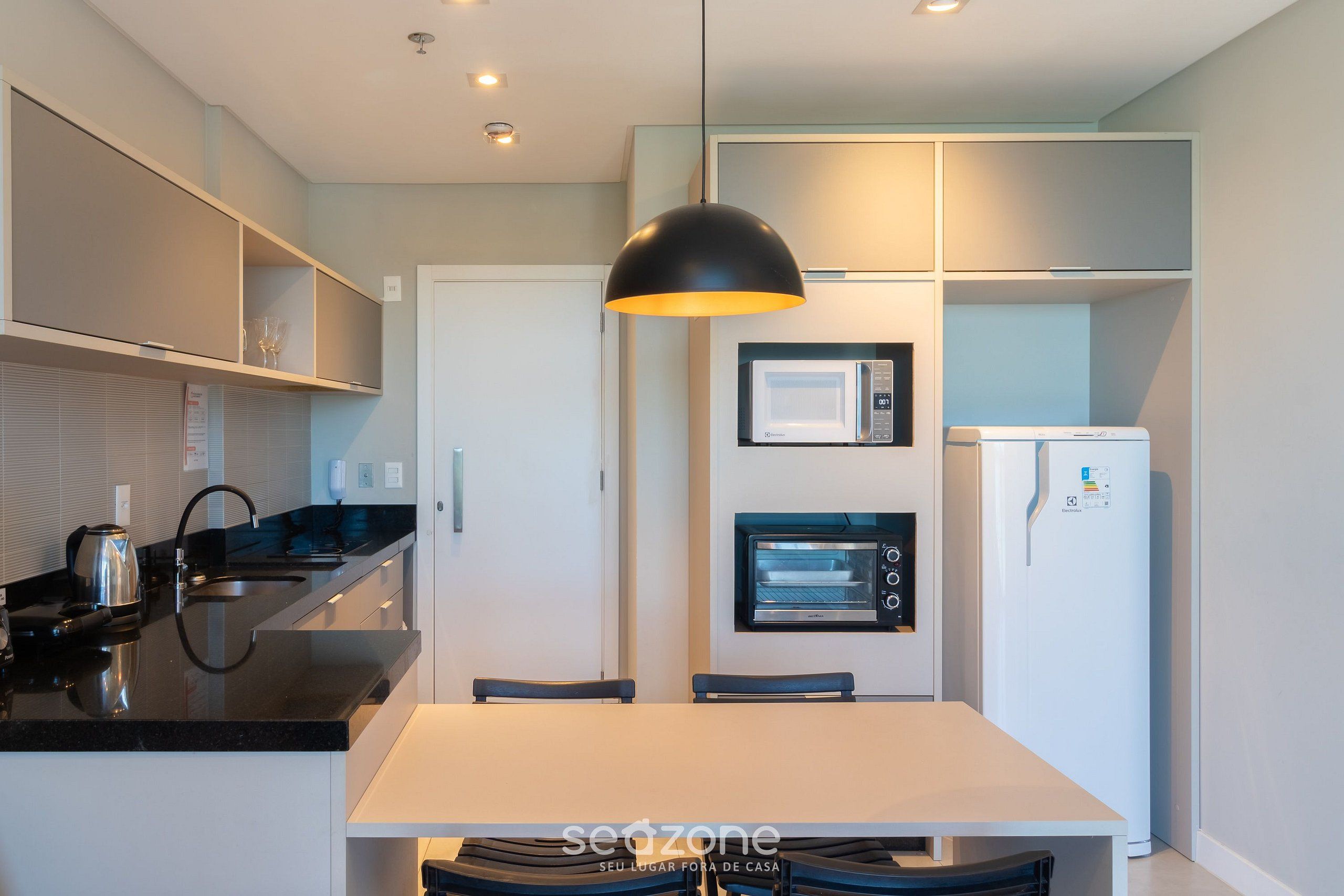 A modern kitchen with a white countertop, black appliances, and a pendant light.