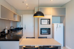 Una cocina moderna con encimera blanca, electrodomésticos negros y una lámpara colgante.