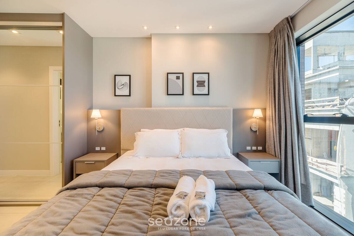 A modern hotel room with a large bed, two bedside lamps, and a window with a view of the city.