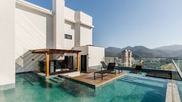 Un edificio moderno con piscina infinita en la azotea, asientos al aire libre y vistas a la montaña.