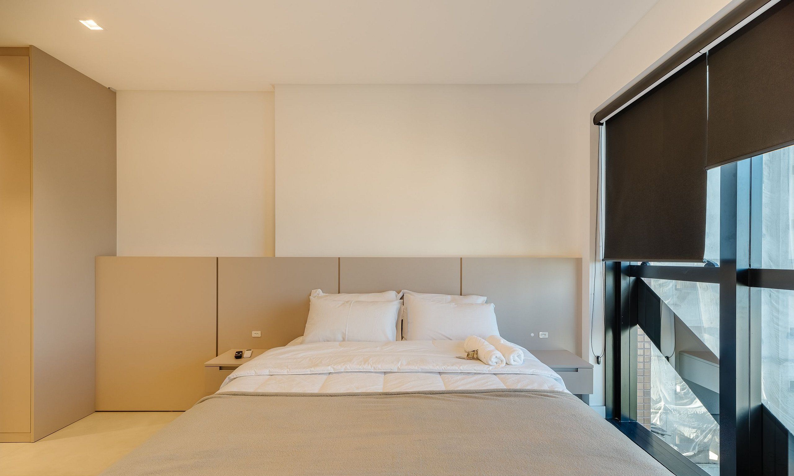 A modern bedroom with a large bed, a bedside table, and a window.