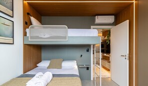 Een kleine hotelkamer met een stapelbed, een klein nachtkastje, een luchtverkoeler aan de muur en een deur naar een badkamer.