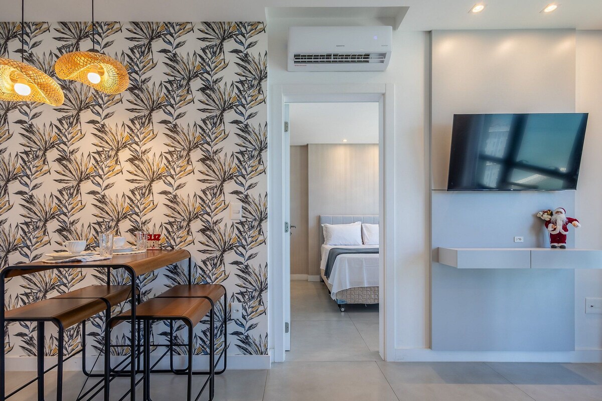 A modern hotel room with a dining area, a bed, a TV, and an air conditioning unit.