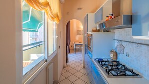 A narrow kitchen with a gas stove, cabinets, and a window with curtains.