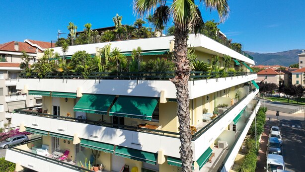 A multi-story hotel with balconies, outdoor seating, and a palm tree.