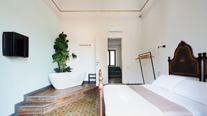 Una camera d'albergo con un letto, una grande pianta in vaso, una TV a schermo piatto e un pavimento in legno.