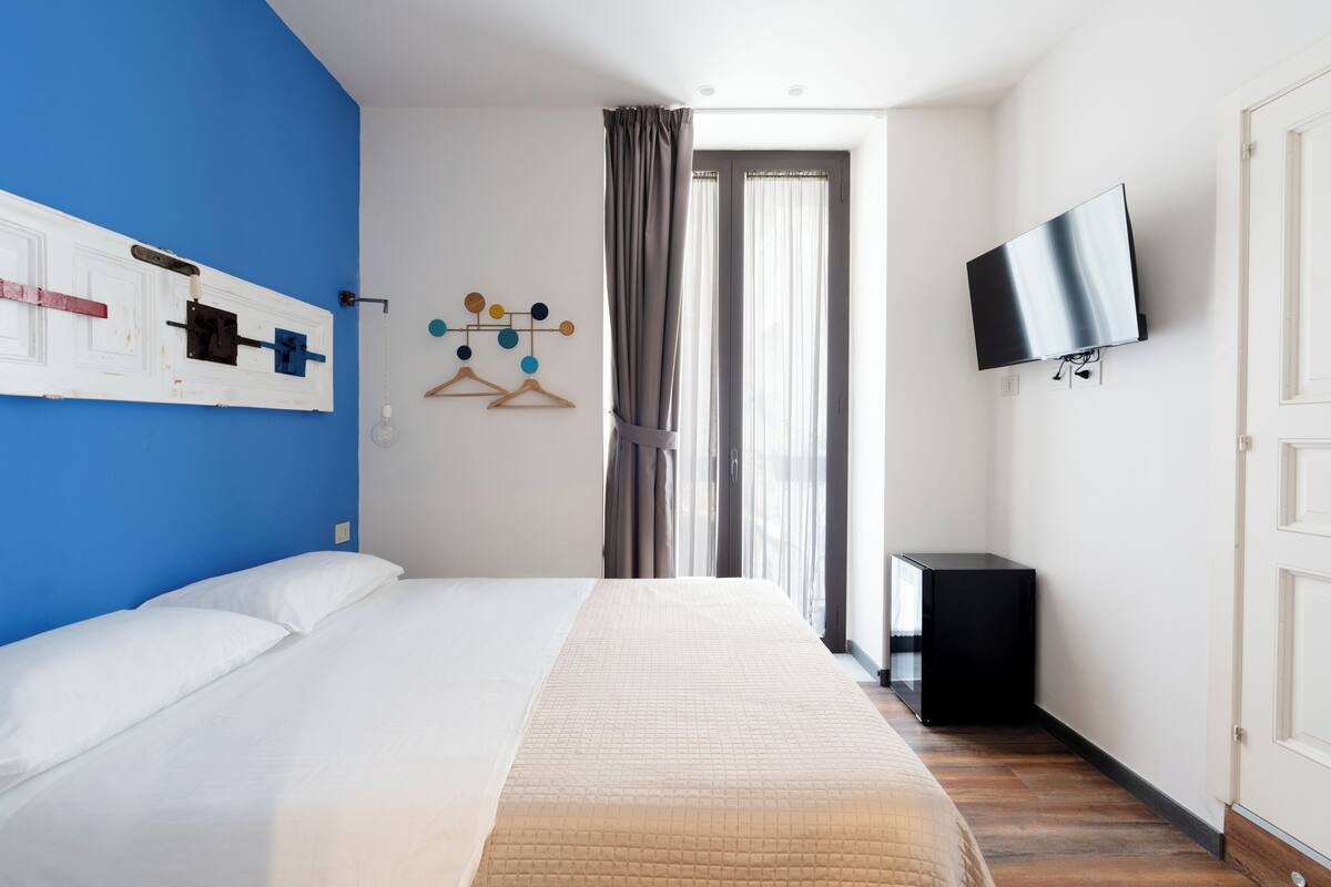 A hotel room with a bed, a TV, a wardrobe, and a window with curtains.