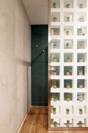 A bathroom with marble walls, a dark green accent wall, and a wooden floor. There is a white shelf unit with potted plants. - Holiday Lux Boutique Room  (Catania)