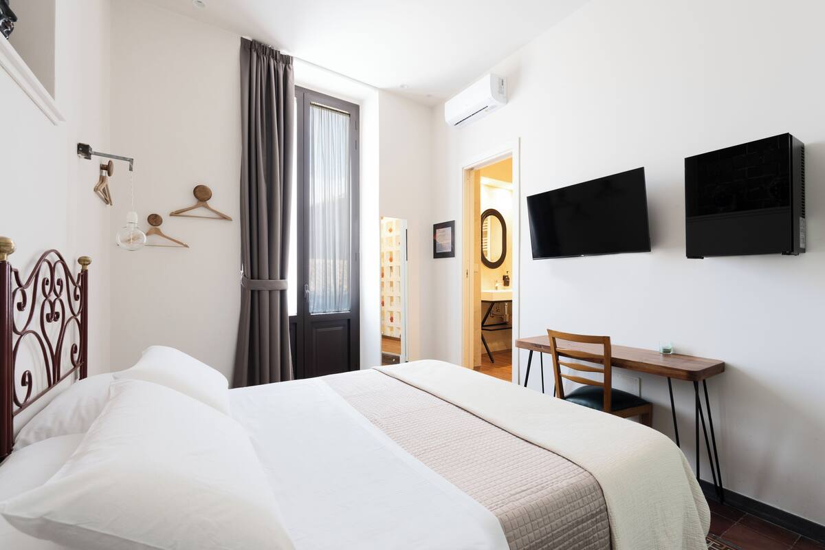 A hotel room with a bed, a desk, a chair, a TV, and a wardrobe.