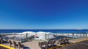Une vue sur la côte, avec une rambarde, des bancs et un navire de croisière au loin.