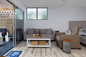 Ein modernes Wohnzimmer mit einem grauen Sofa, einem weißen Couchtisch, Korbmöbeln und einem großen Fenster.