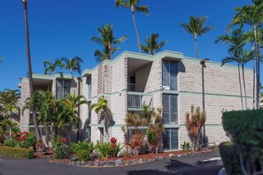 Un hotel de varios pisos con fachada de ladrillo, balcones y jardines tropicales.