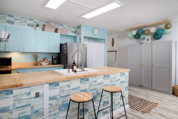Una cocina moderna con armarios azul claro, encimera de madera, dos taburetes, un refrigerador y un reloj en la pared.