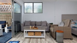 Un salon moderne avec un canapé gris, une table basse blanche, des meubles en osier et une grande fenêtre.