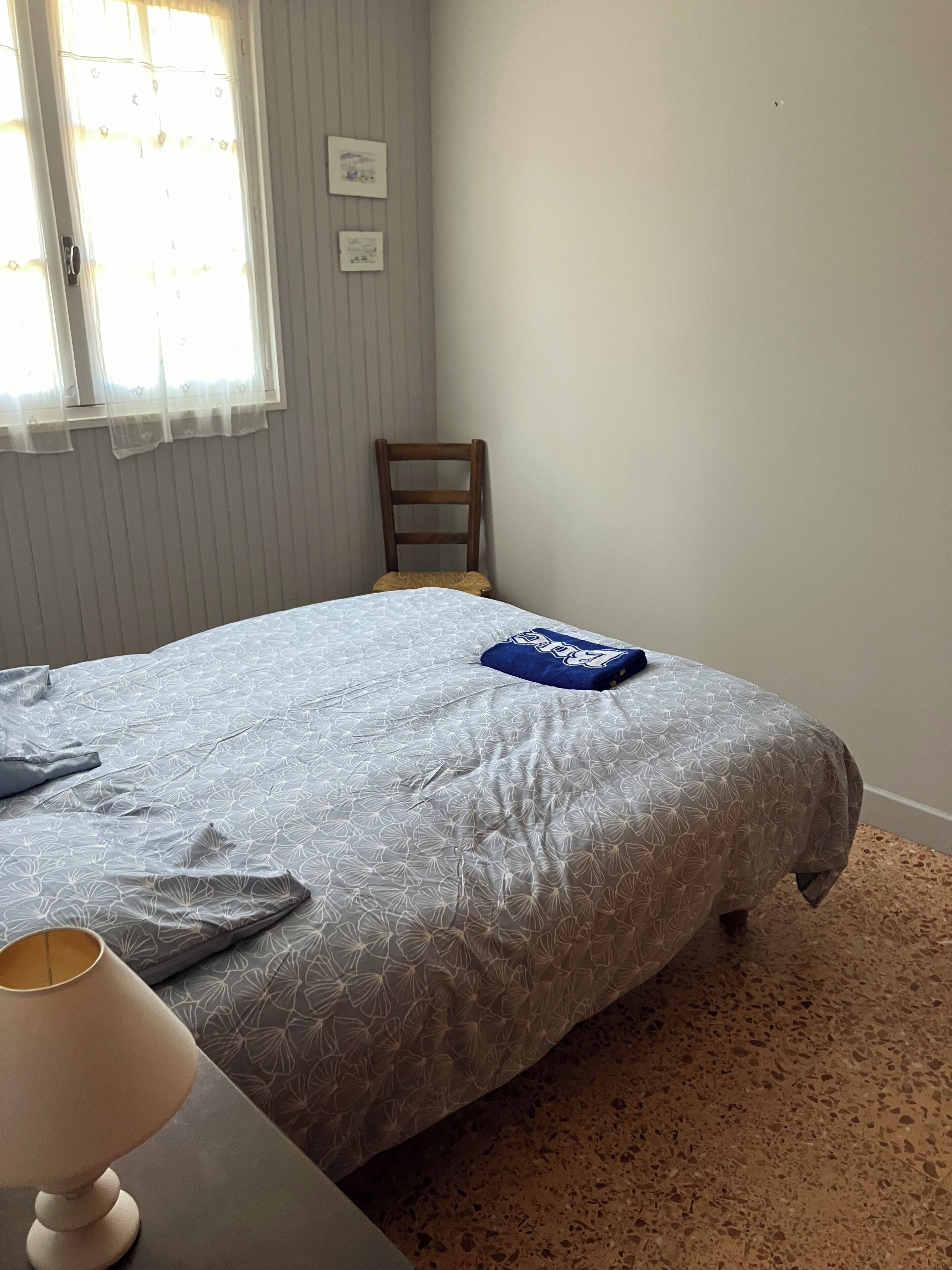 Une chambre à coucher avec un lit, une chaise, une lampe et une fenêtre avec des stores.