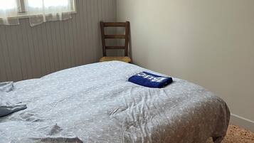 Une chambre à coucher avec un lit, une chaise, une lampe et une fenêtre avec des stores.