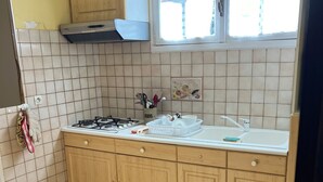 A kitchen with wooden cabinets, a gas stove, a sink, and a window with blinds. - Gîte du Puy des Gardes (Meymac)